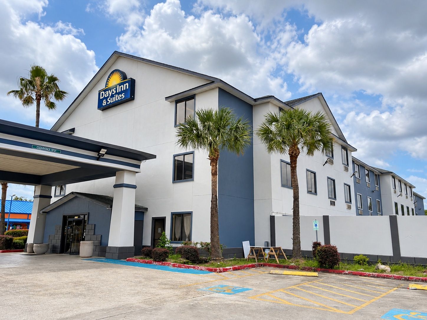 A Days Inn & Suites building with a clear sky, palm trees, and a parking lot.