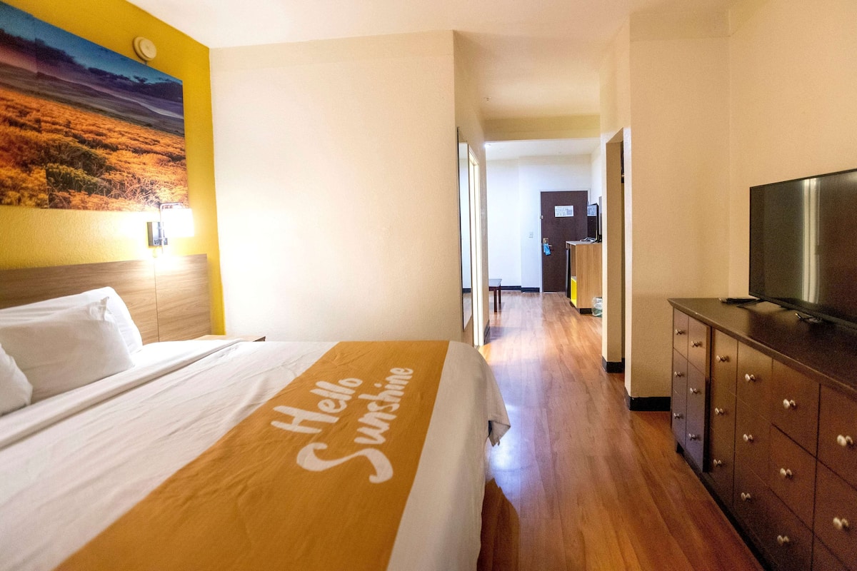 Ein Hotelzimmer mit einem Bett, einem Fernseher, einer Holzkommode und einem Flur, der zu einem anderen Zimmer führt.