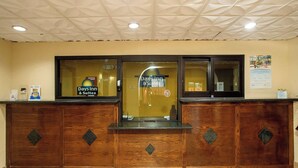 A reception desk with a glass partition, a sign for Days Inn & Suites, and a bulletin board on the wall. - Days Inn & Suites by Wyndham Houston North/Aldine (Houston)