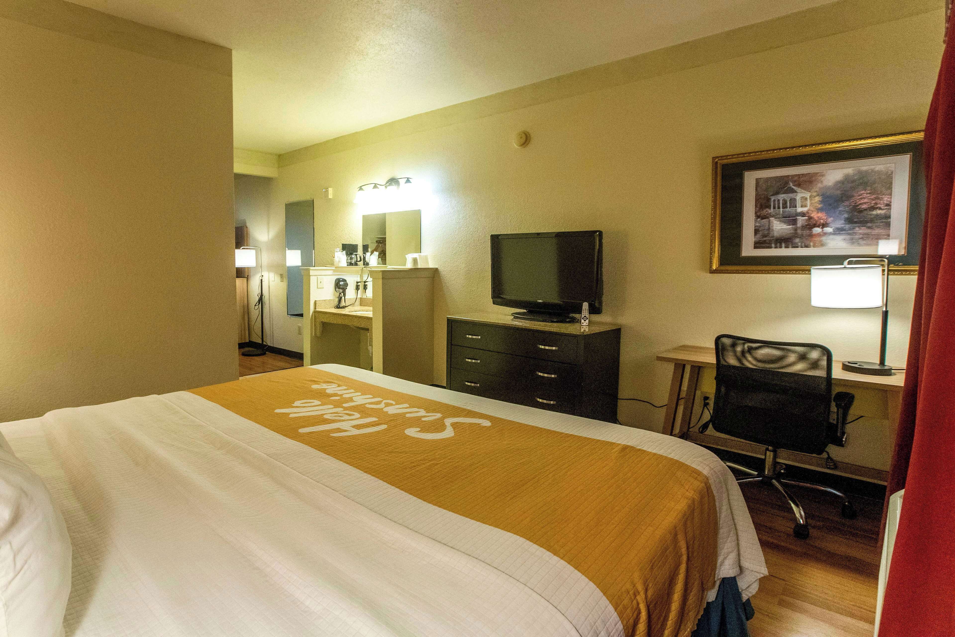 Una habitación de hotel con cama, escritorio, silla, televisión y un cuadro en la pared.