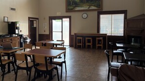 A dining area with tables and chairs, a painting on the wall, a clock, and a water dispenser. - Days Inn & Suites by Wyndham Houston North/Aldine (Houston)