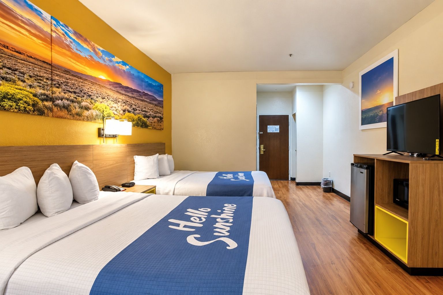 Camera d'albergo con due letti, televisione, scrivania e un quadro raffigurante un tramonto.