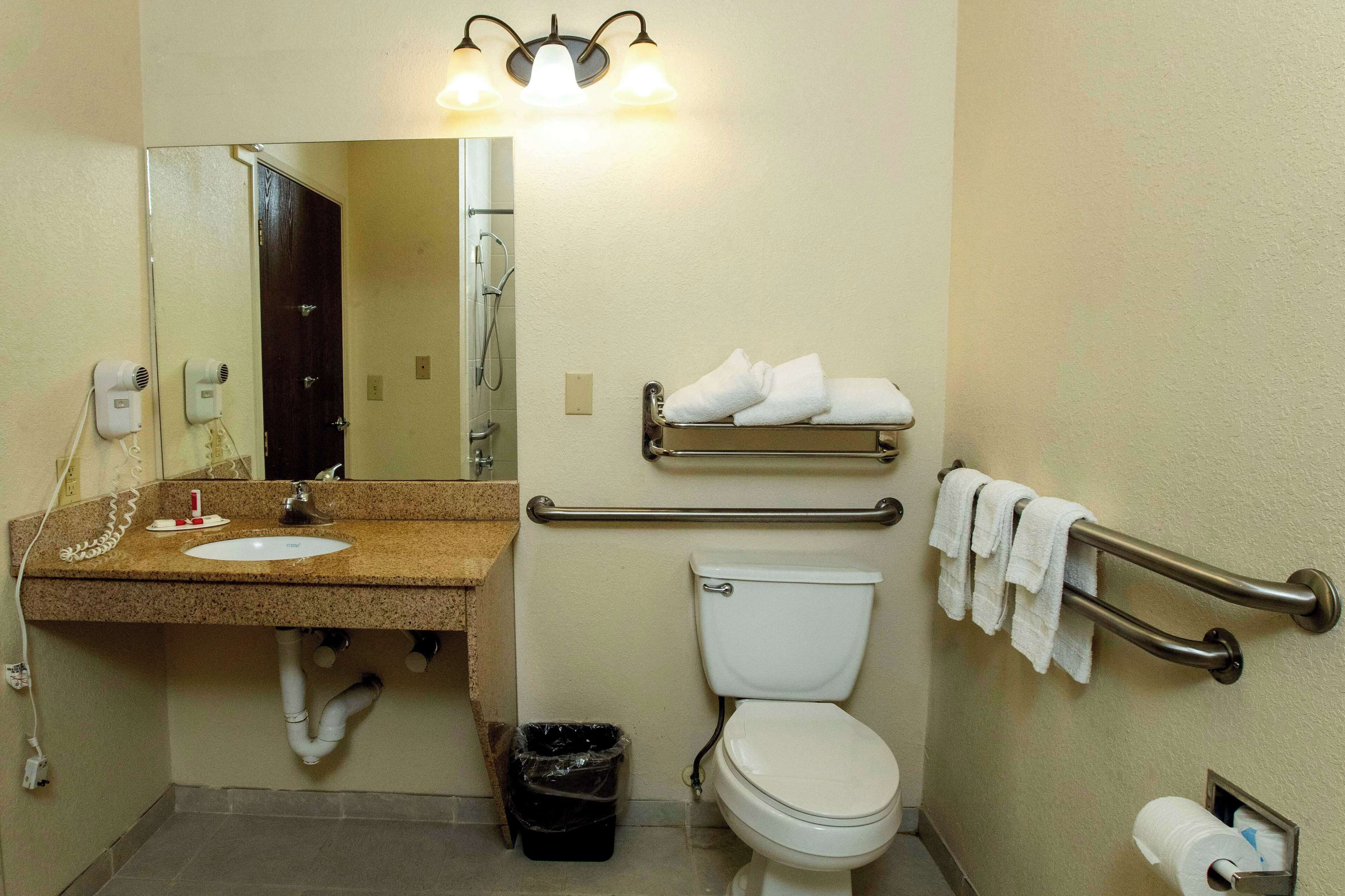 A bathroom with a sink, mirror, towel rack, toilet, and a trash bin.