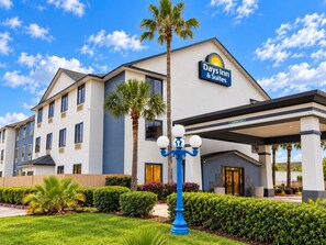 A Days Inn & Suites building with a clear sky, palm trees, and a blue street lamp. - Days Inn & Suites by Wyndham Houston North/Aldine (Houston)
