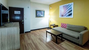 A living room with a sofa, a coffee table, a lamp, and a television. - Days Inn & Suites by Wyndham Houston North/Aldine (Houston)