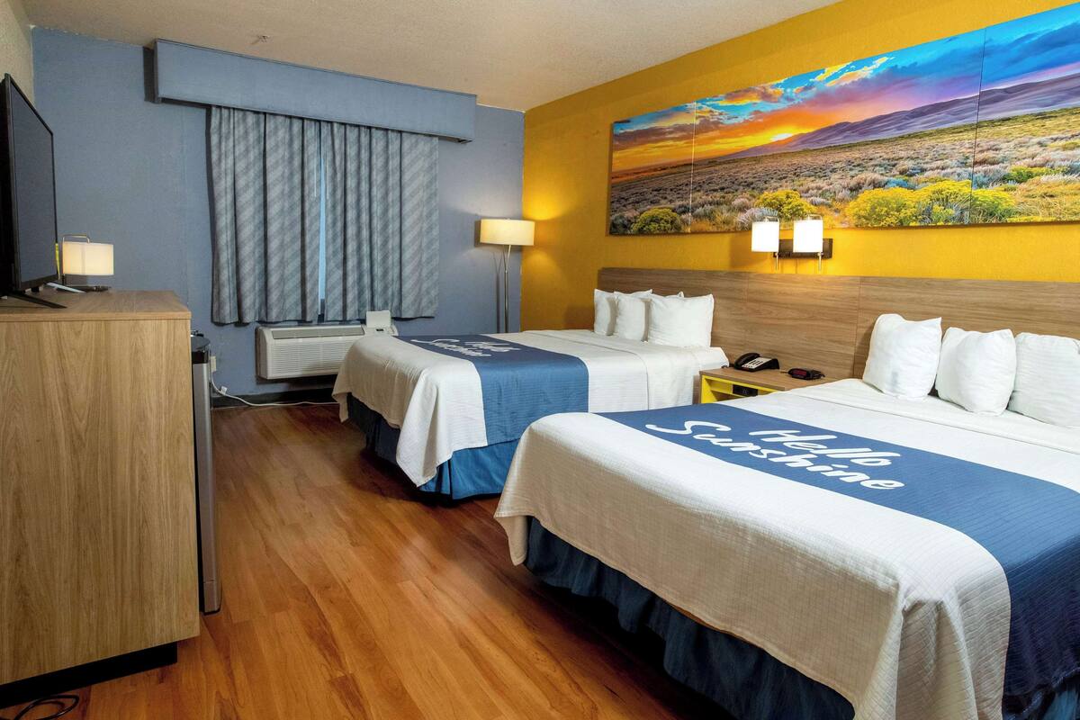 Ein Hotelzimmer mit zwei Betten, einem Fernseher, einem Schreibtisch und einem Bild an der Wand.