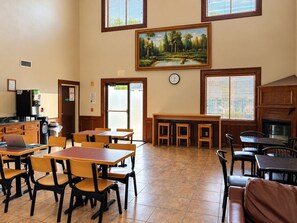 A dining area with wooden tables and chairs, a painting above the tables, and a clock on the wall. - Days Inn & Suites by Wyndham Houston North/Aldine (Houston)