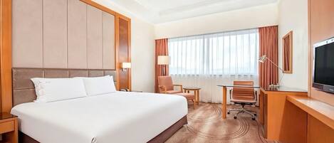 A hotel room with a large bed, a desk, a chair, a TV, and a window with curtains.