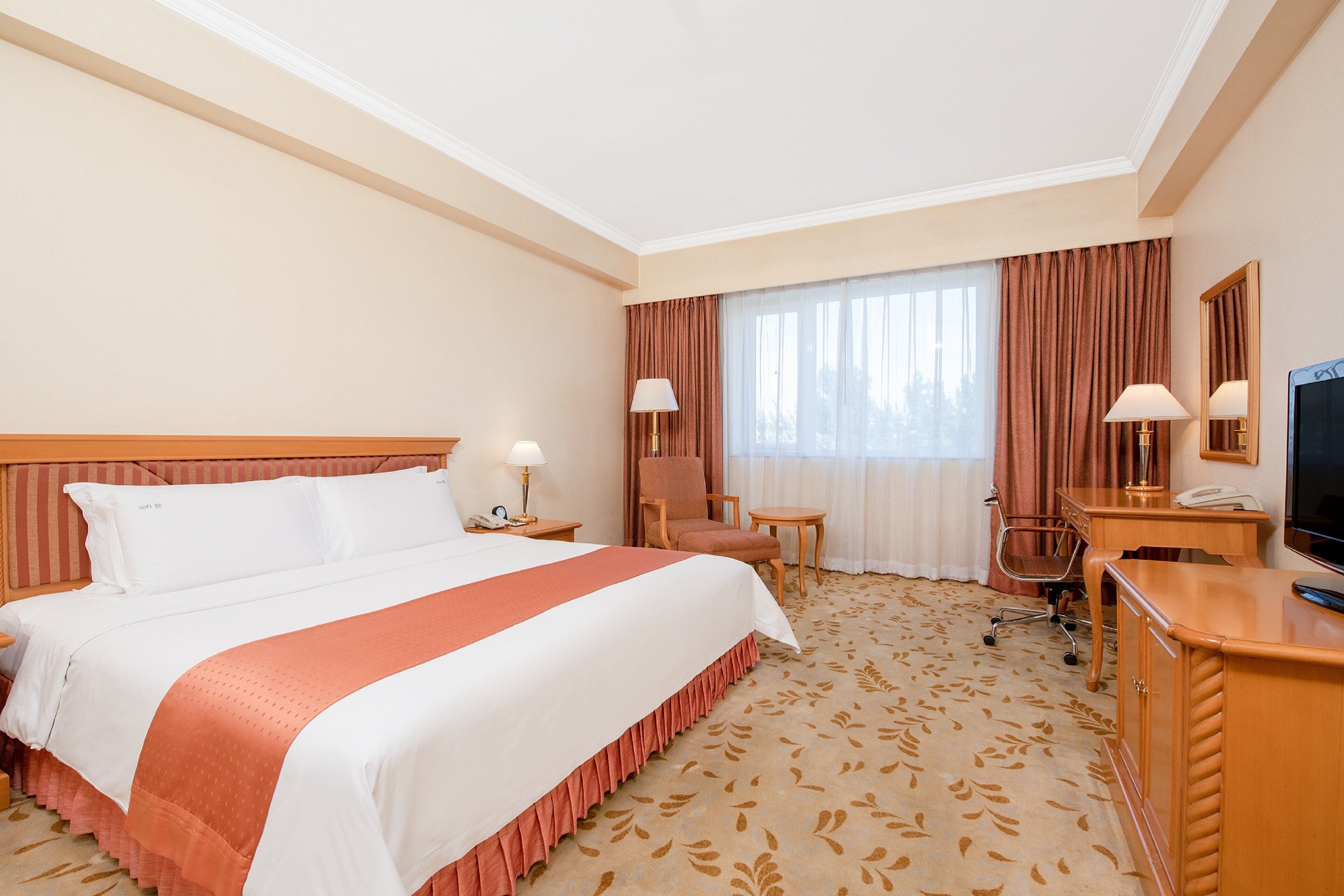 Habitación de hotel con una cama grande, un escritorio, una silla, un televisor y un ventanal con cortinas.
