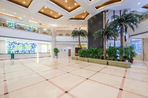 A spacious lobby with a high ceiling, a central column, and a seating area with planters. - Holiday Inn Beijing Chang An West by IHG (Beijing)