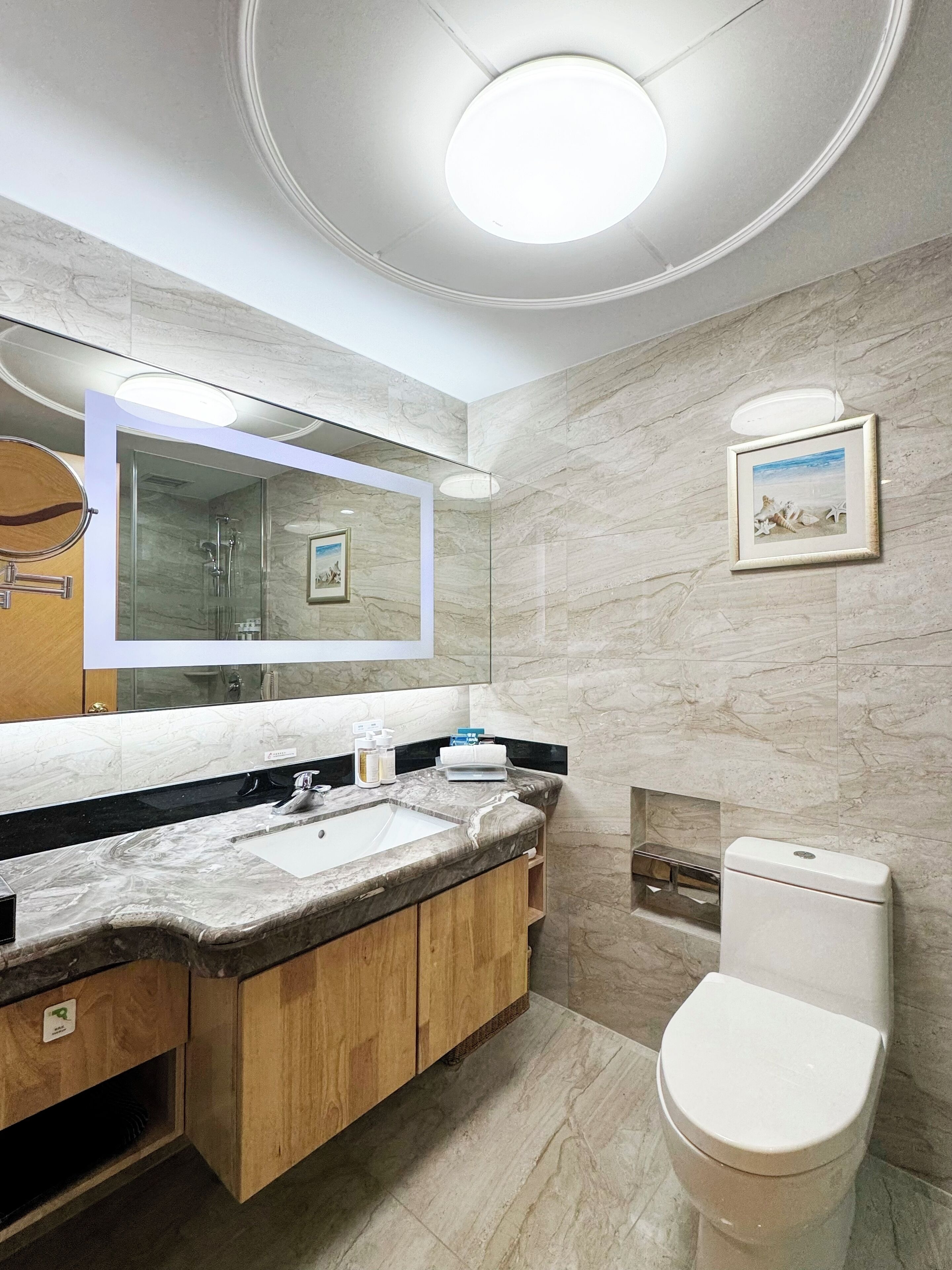 Une salle de bain moderne avec un lavabo en marbre, des meubles en bois, une cabine de douche en verre et des toilettes.