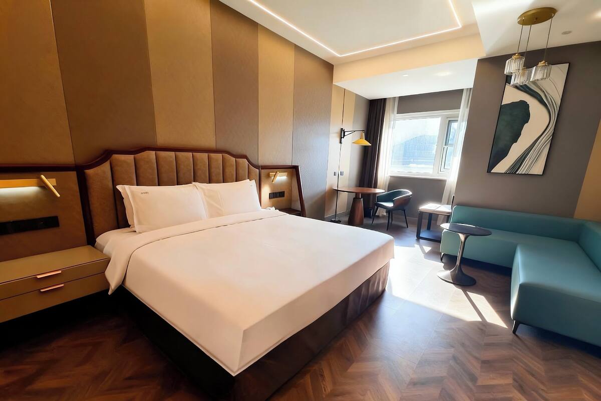 A modern hotel room with a large bed, a sofa, a small table, and a chair.