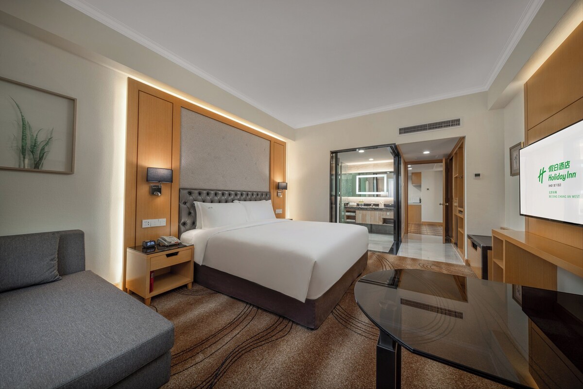 A hotel room with a large bed, a sofa, a desk, and a TV.
