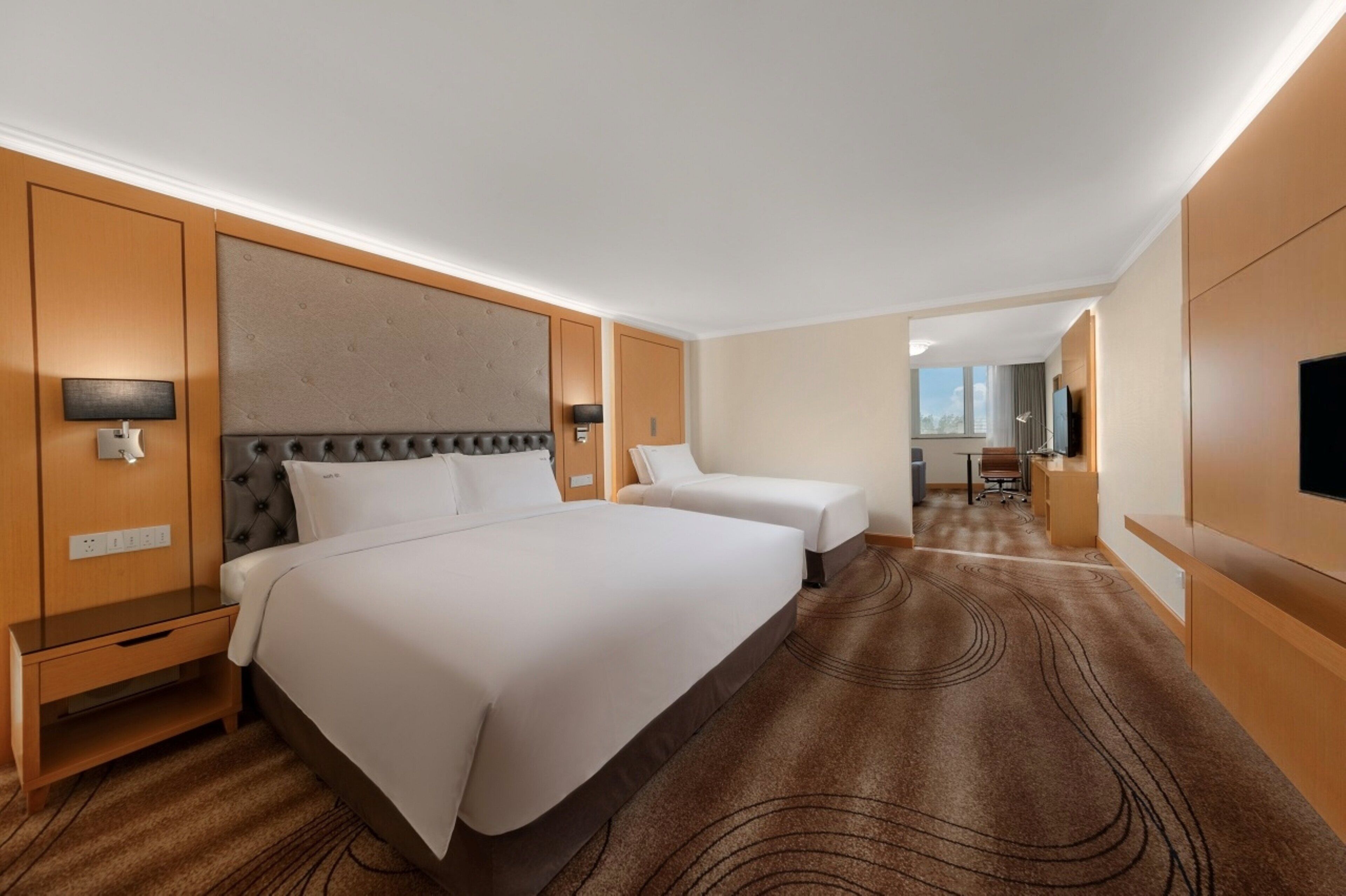 Ein Hotelzimmer mit einem großen Bett, einem kleineren Bett, einem Schreibtisch und einem Fernseher.