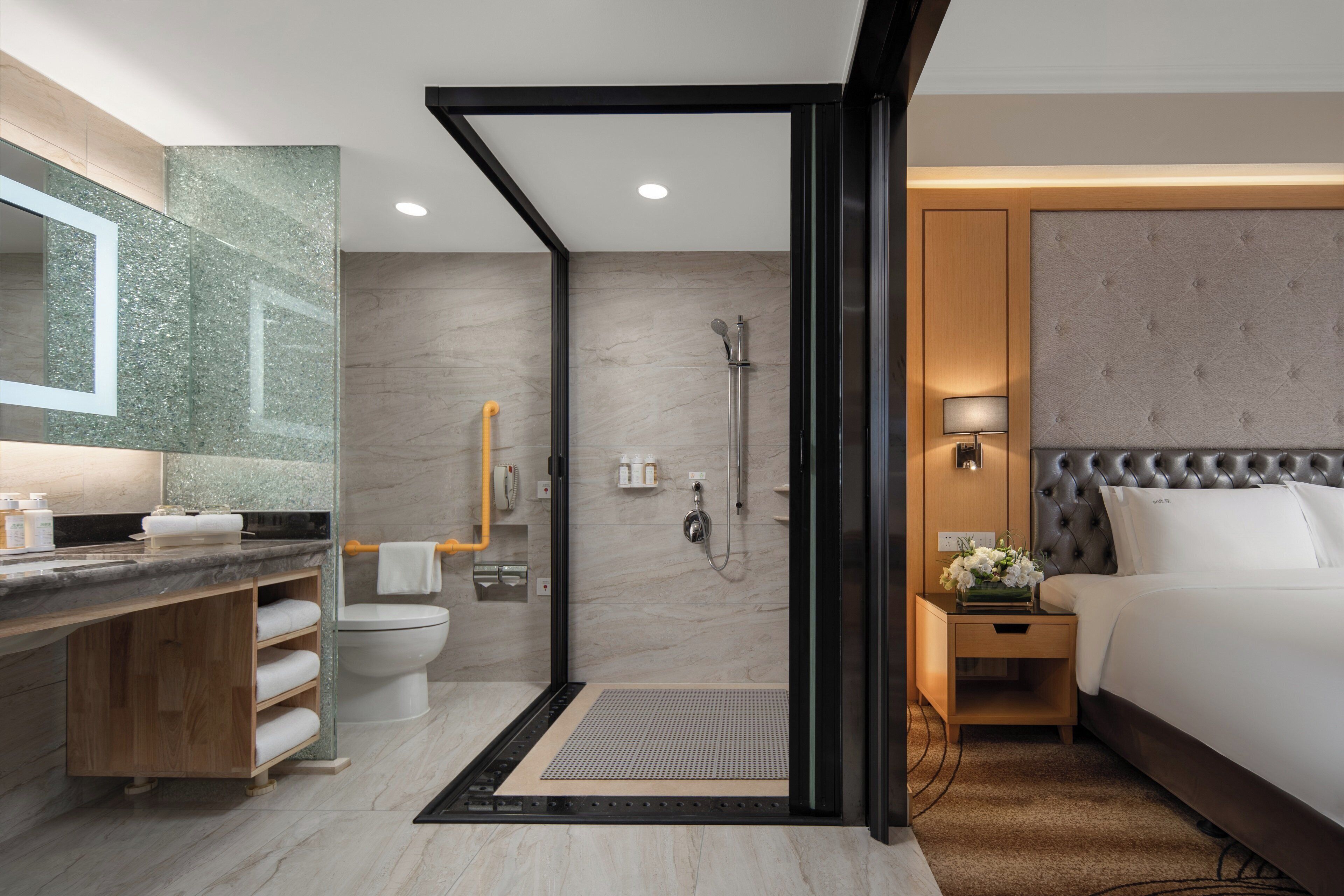 Un baño moderno de hotel con ducha, inodoro y tocador con espejo.