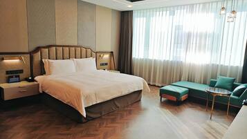 Ein modernes Hotelzimmer mit einem großen Bett, einem grünen Sofa, einem kleinen Tisch und einem Nachttisch mit einer Lampe.