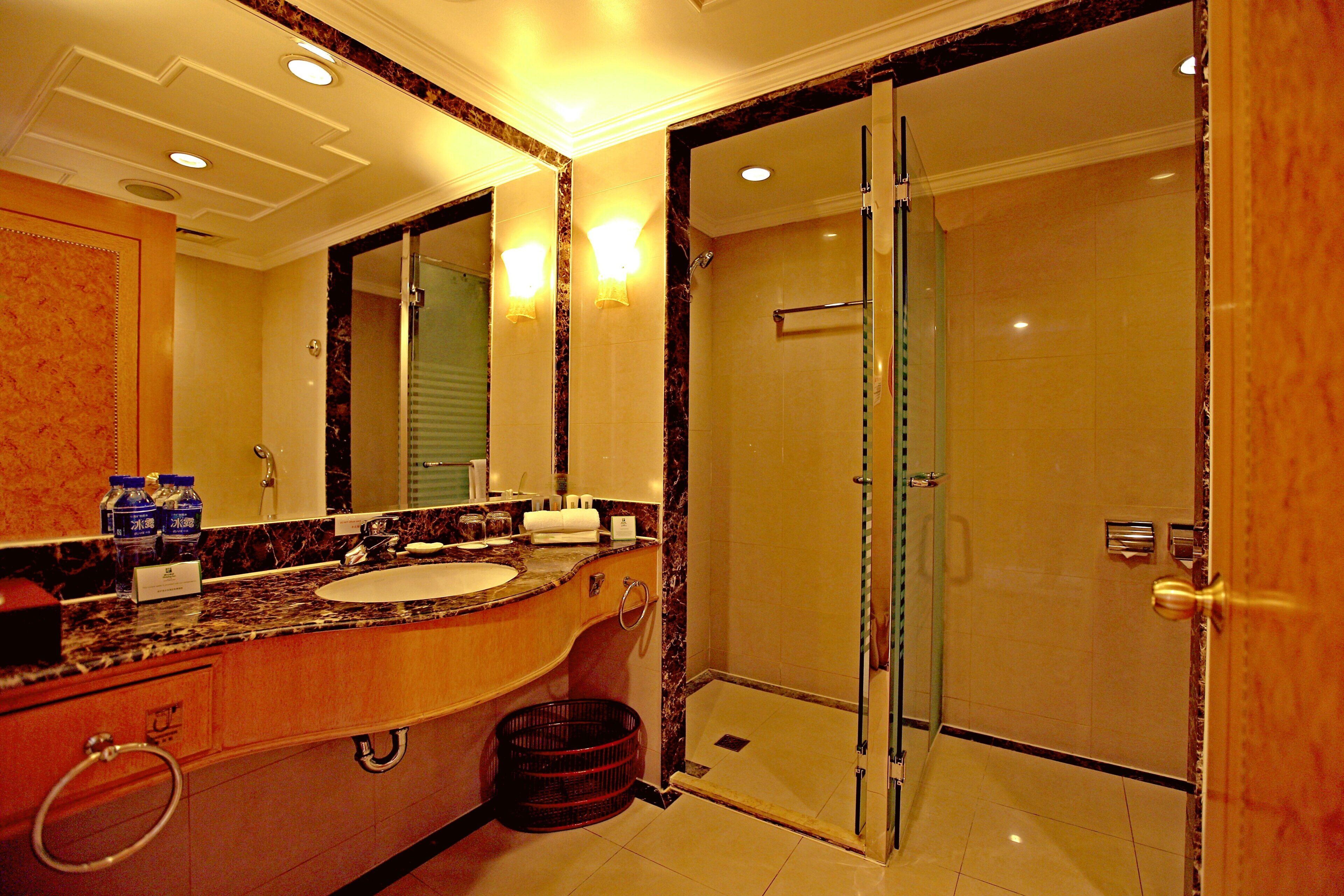 A hotel bathroom with a marble vanity, a glass shower enclosure, and a large mirror.