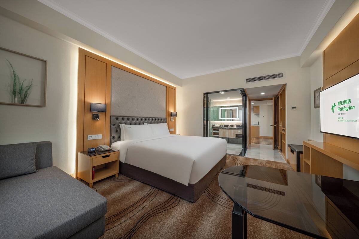 A hotel room with a large bed, a sofa, a desk, and a TV.
