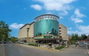 A modern hotel with a curved glass facade, multiple floors, and a prominent entrance with flags. - Holiday Inn Beijing Chang An West by IHG (Beijing)