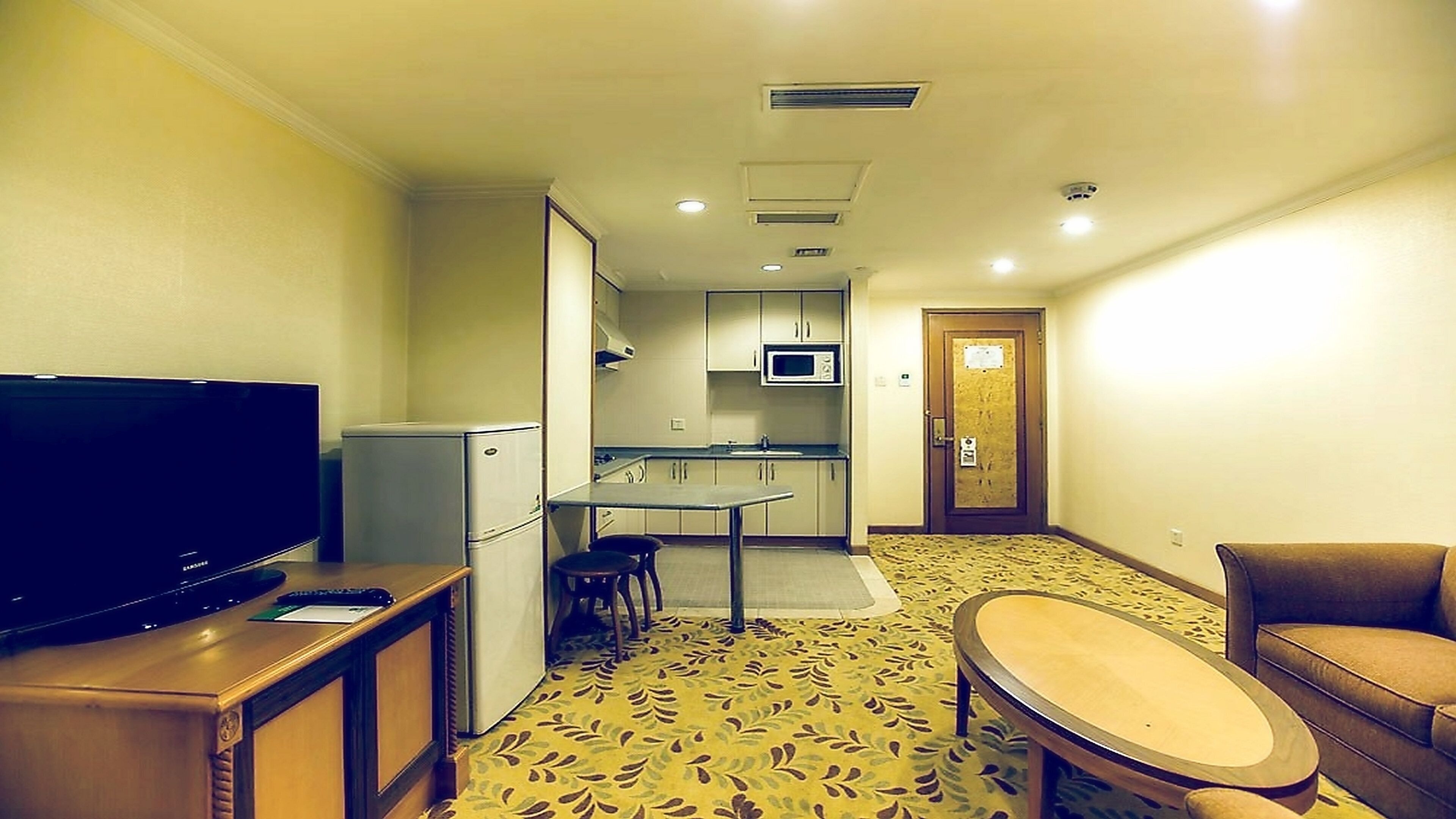 A compact hotel room with a television, kitchenette, dining area, and seating.