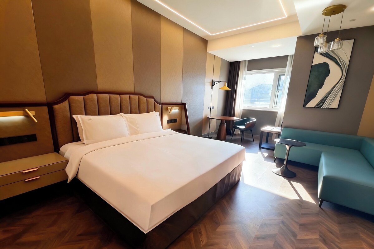 A modern hotel room with a large bed, a sofa, a small table, and a chair.