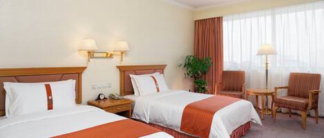 A hotel room with two beds, a nightstand, a chair, a table, and a large window with curtains.