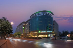 A modern hotel with a curved glass facade, multiple floors, and a prominent entrance with signage. - Holiday Inn Beijing Chang An West by IHG (Beijing)