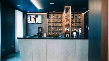Una zona de bar con mostrador, estantes llenos de botellas y una pantalla de televisión.