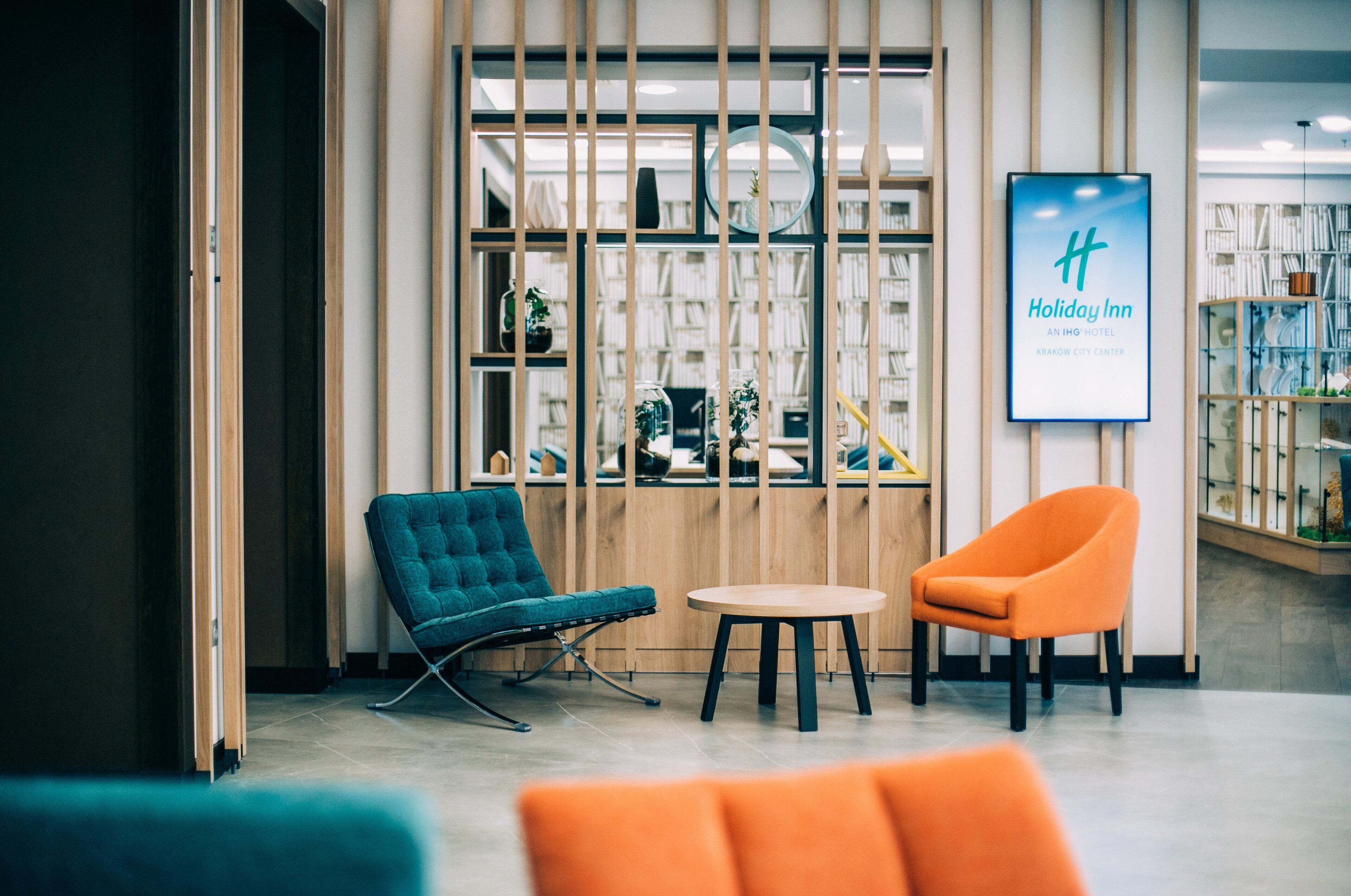 Un vestíbulo moderno de hotel con un mostrador de recepción de madera, un sillón azul, un sillón naranja y una mesa redonda.