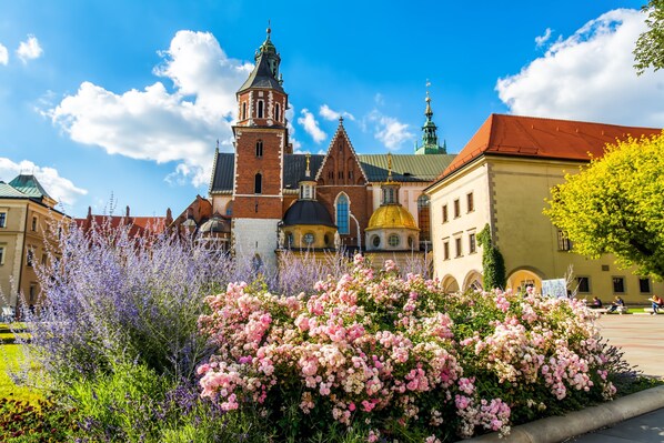 A historic building with a prominent tower and domed architecture, surrounded by lush flowering plants.