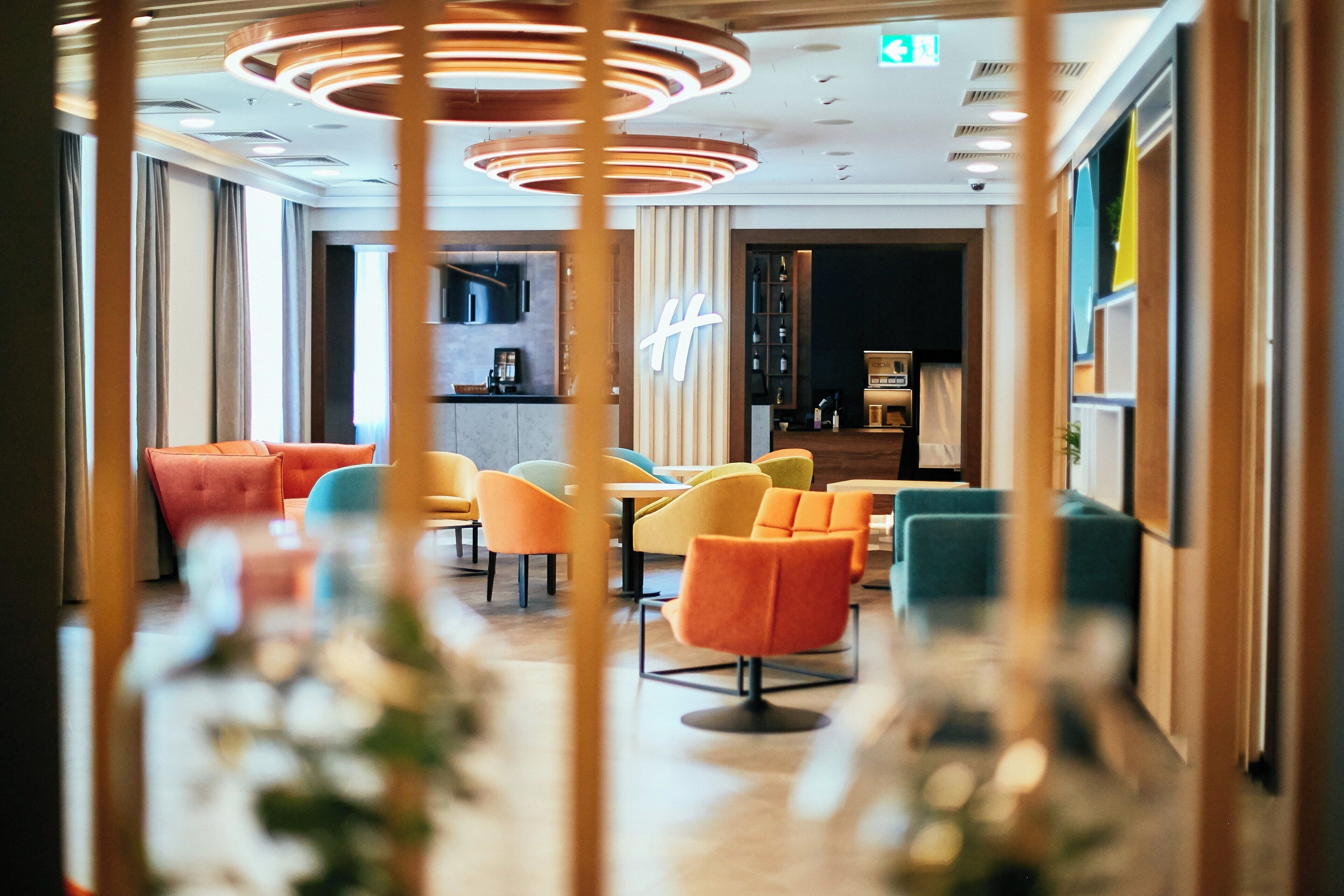 A modern hotel lobby with a seating area, a bar, and a kitchen in the background.