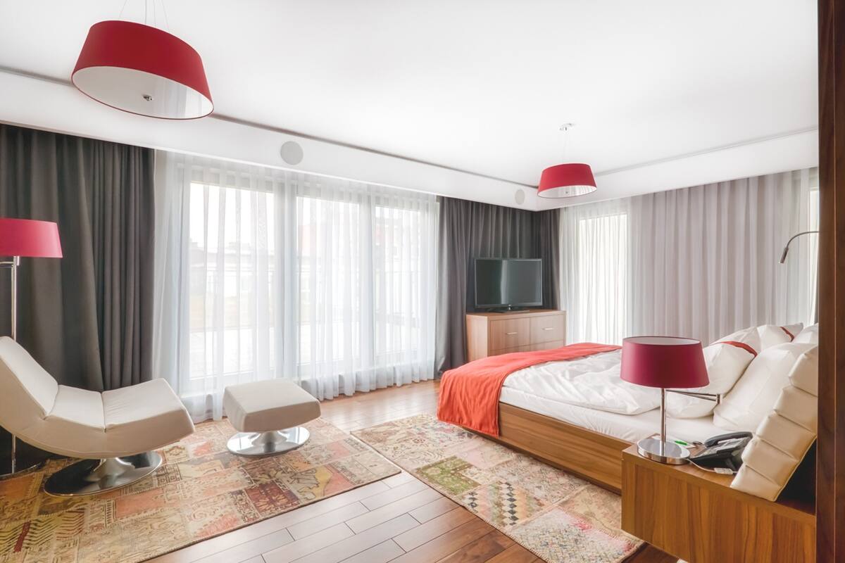 A modern hotel room with a large bed, a TV, a desk, and a chair.