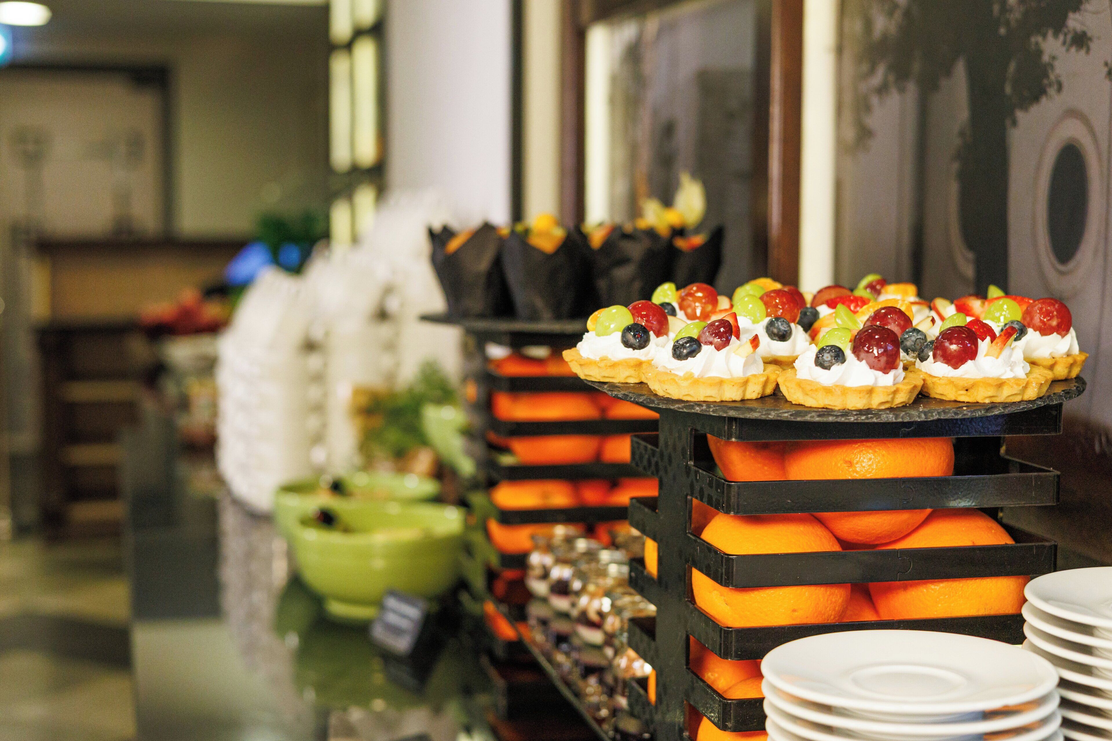 A buffet with fruit-topped desserts and a green bowl in the background.