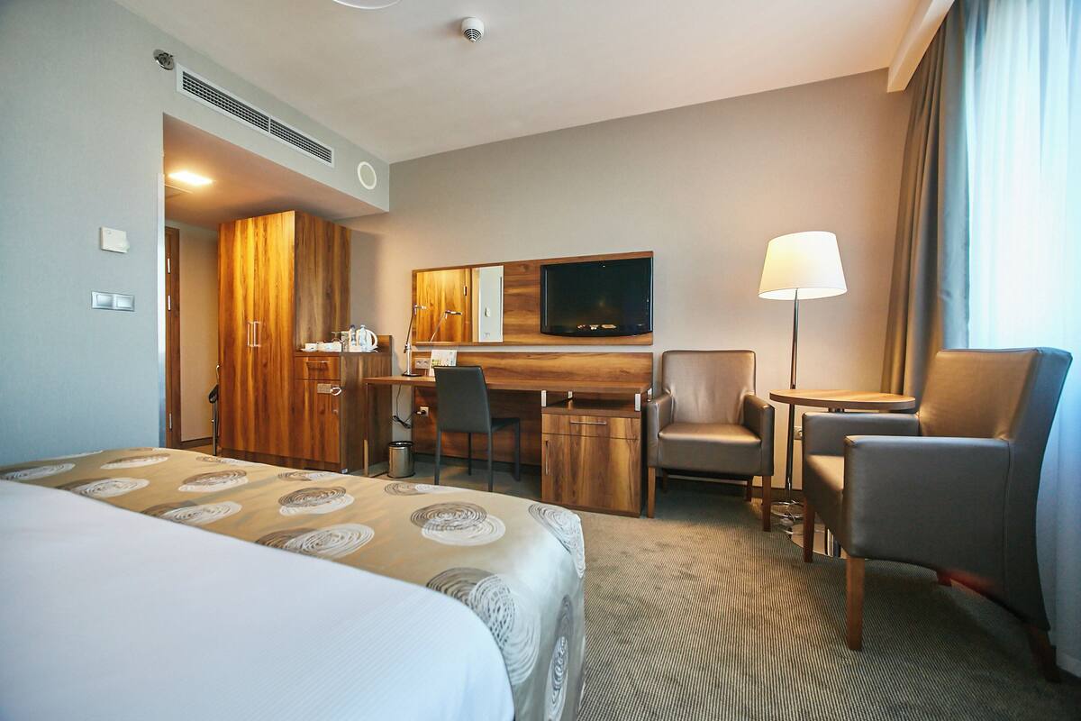 A hotel room with a bed, a desk, a chair, a TV, and a lamp.