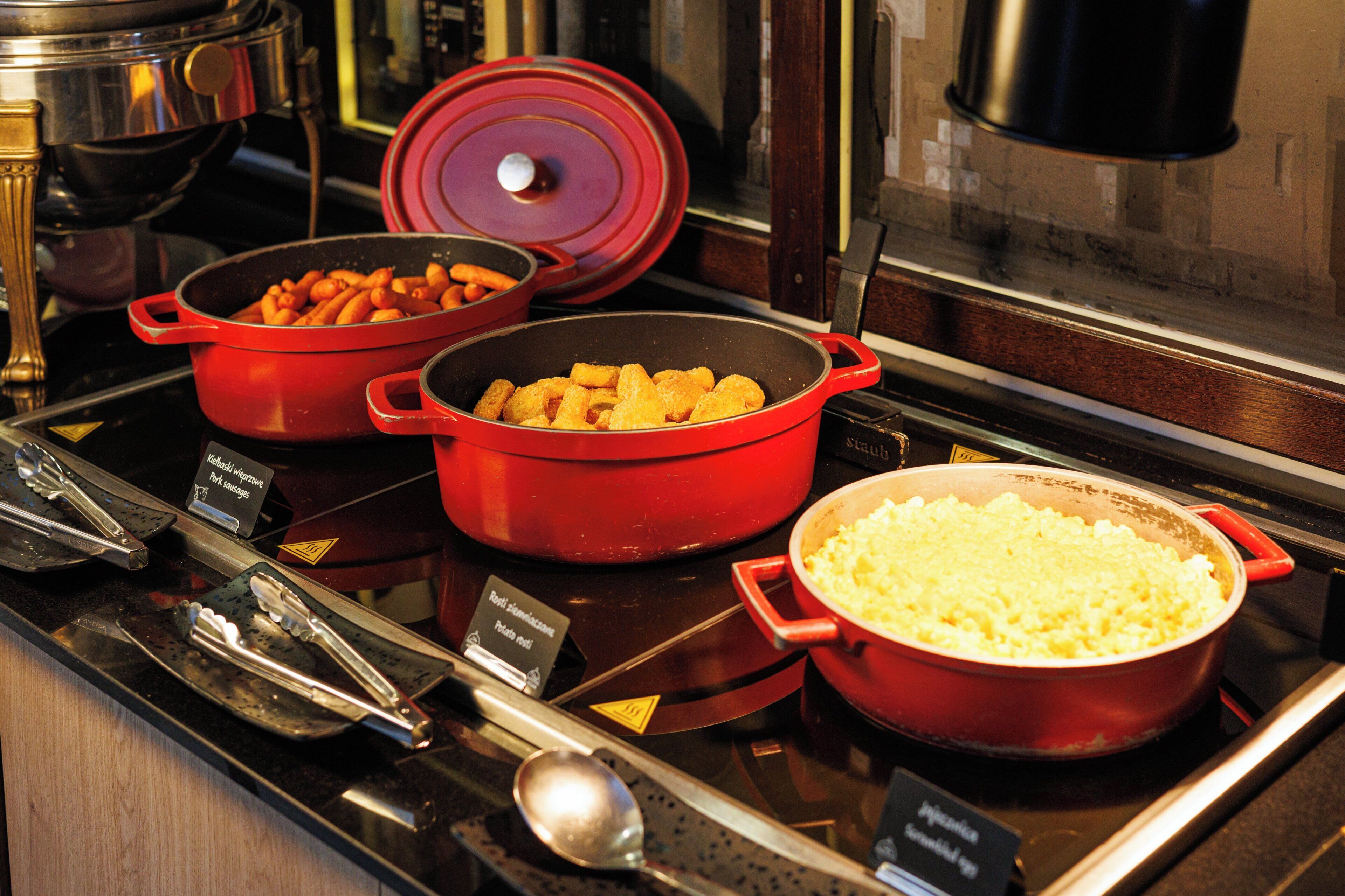 A buffet with various dishes in red pots, including what appears to be pasta, fried items, and a large pot of rice.