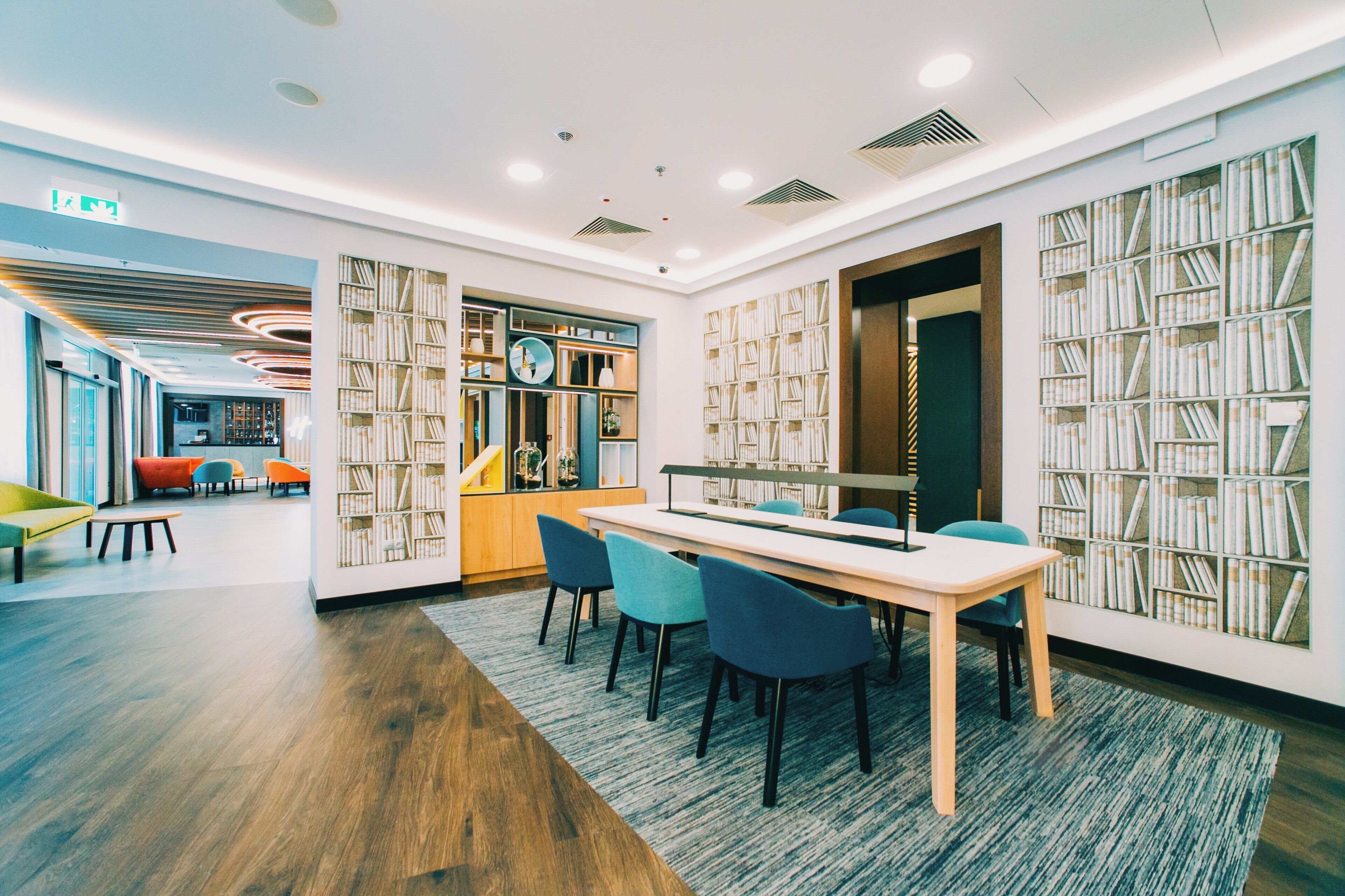 A modern library with a long table, blue chairs, and bookshelves filled with books.