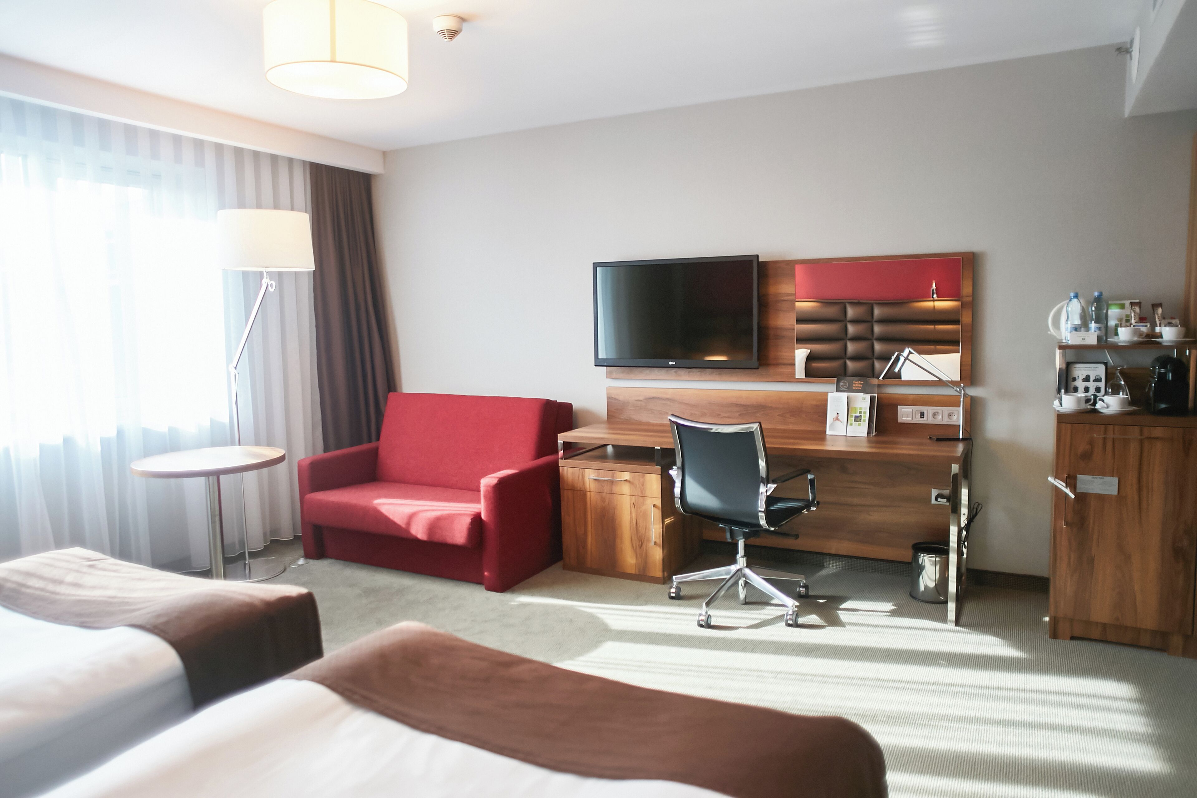 A hotel room with a bed, a desk, a chair, a TV, and a lamp.