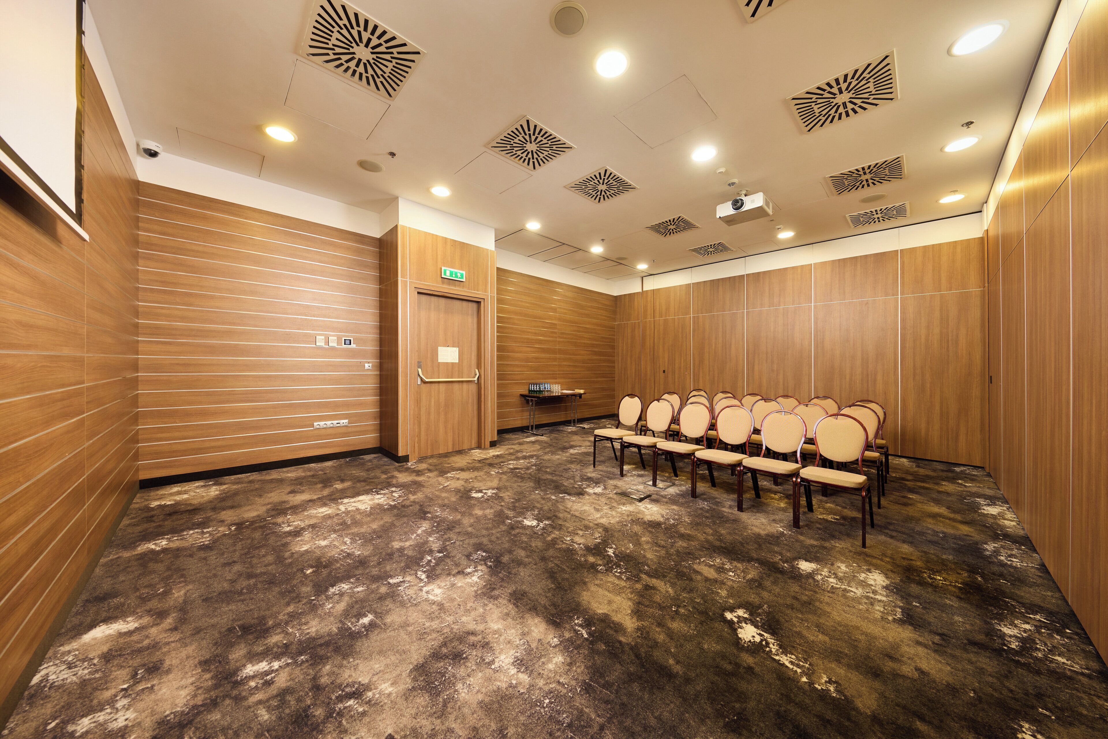 A conference room with a wooden floor, ceiling lights, and a row of chairs.