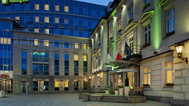 A Holiday Inn hotel with a modern glass facade, a traditional building with a balcony, and a well-lit entrance area. - Holiday Inn Krakow City Centre by IHG (Kraków)