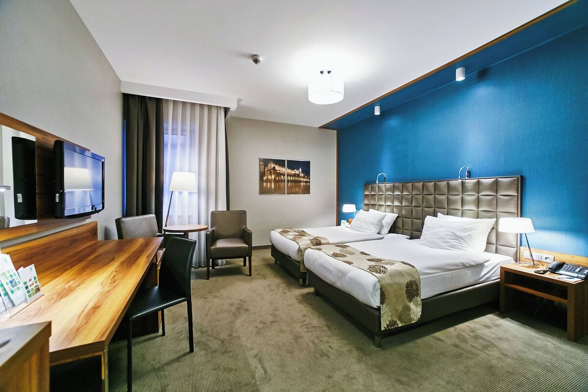 A hotel room with a large bed, a desk, a chair, a TV, and a window with curtains.