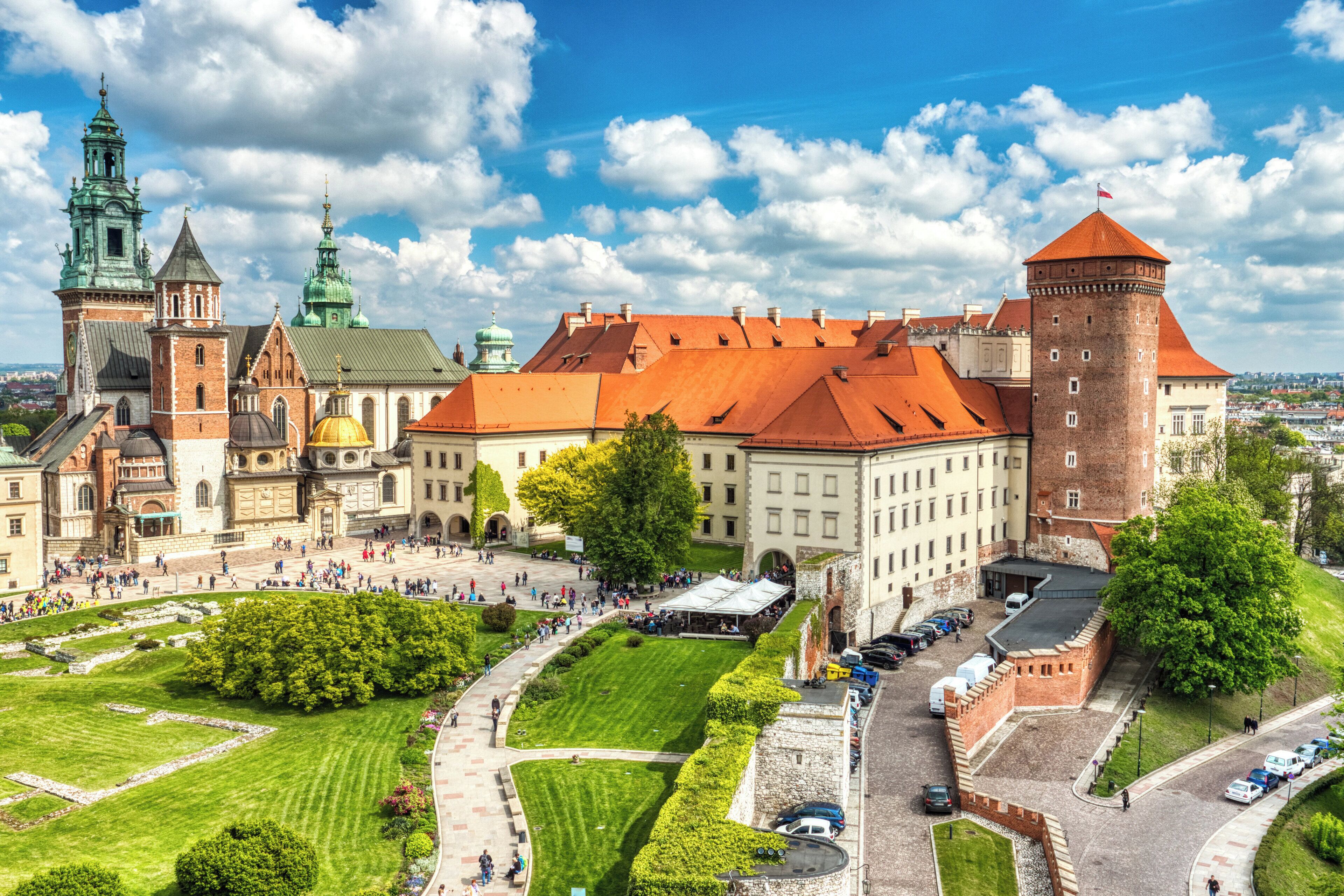 A historic building complex with multiple towers, a central courtyard, and a large open space with a lawn and pathways.
