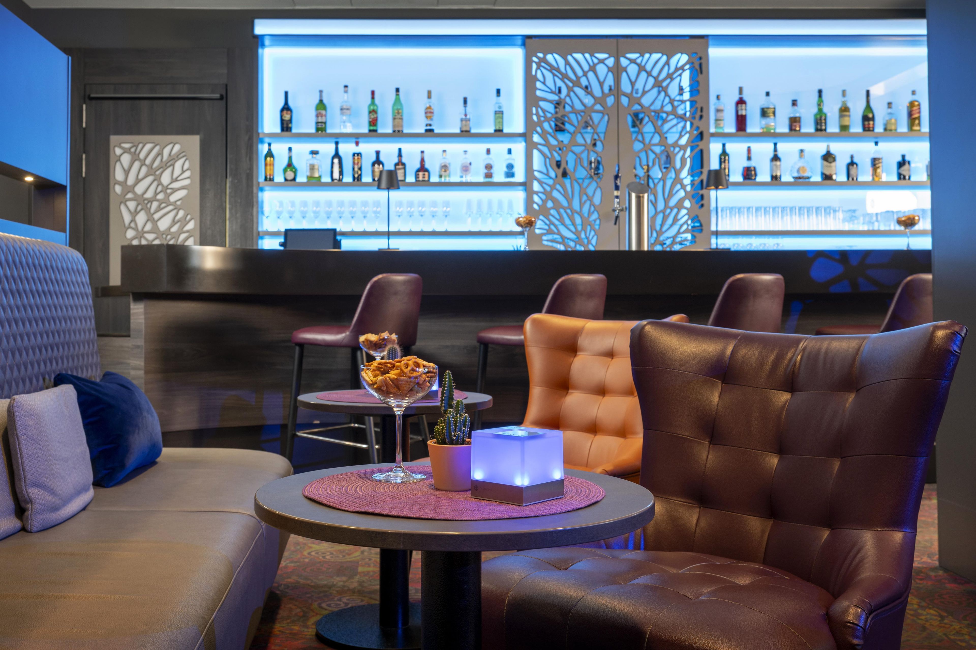 A bar area with leather seating, a small table with a cactus and a glass, and a bar stocked with various bottles.
