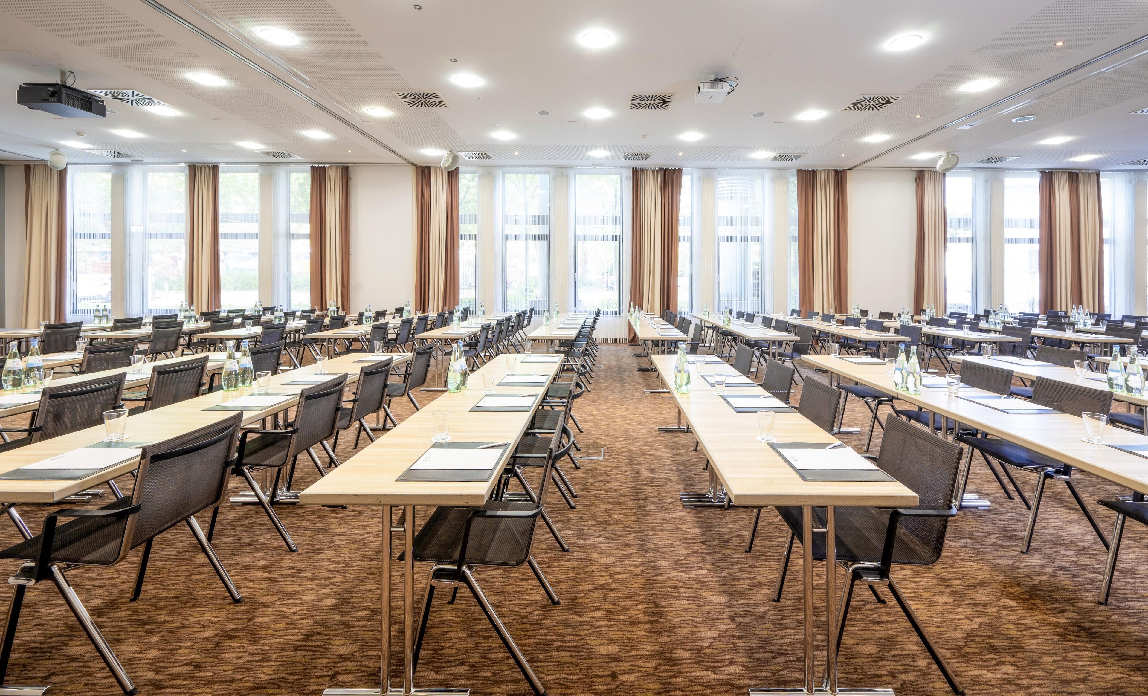 Une salle de conférence dotée de plusieurs tables et chaises, de grandes fenêtres et de projecteurs au plafond.