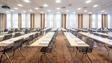 Une salle de conférence dotée de plusieurs tables et chaises, de grandes fenêtres et de projecteurs au plafond.