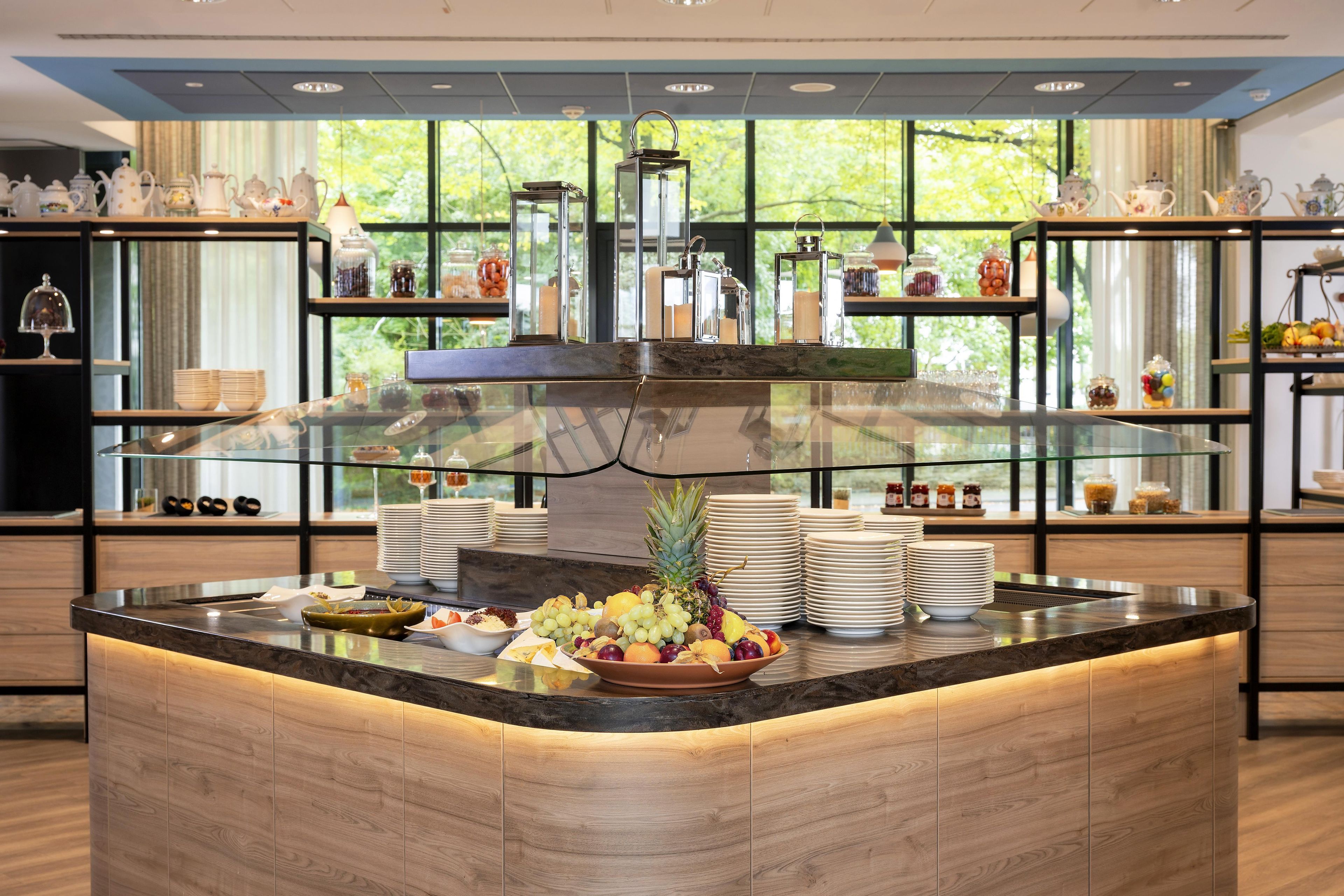 Un buffet de petit-déjeuner proposant une variété de fruits, une vitrine réfrigérée et des étagères où sont exposés des services à thé.