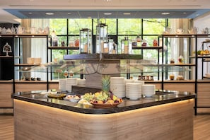 Un buffet de petit-déjeuner proposant une variété de fruits, une vitrine réfrigérée et des étagères où sont exposés des services à thé.