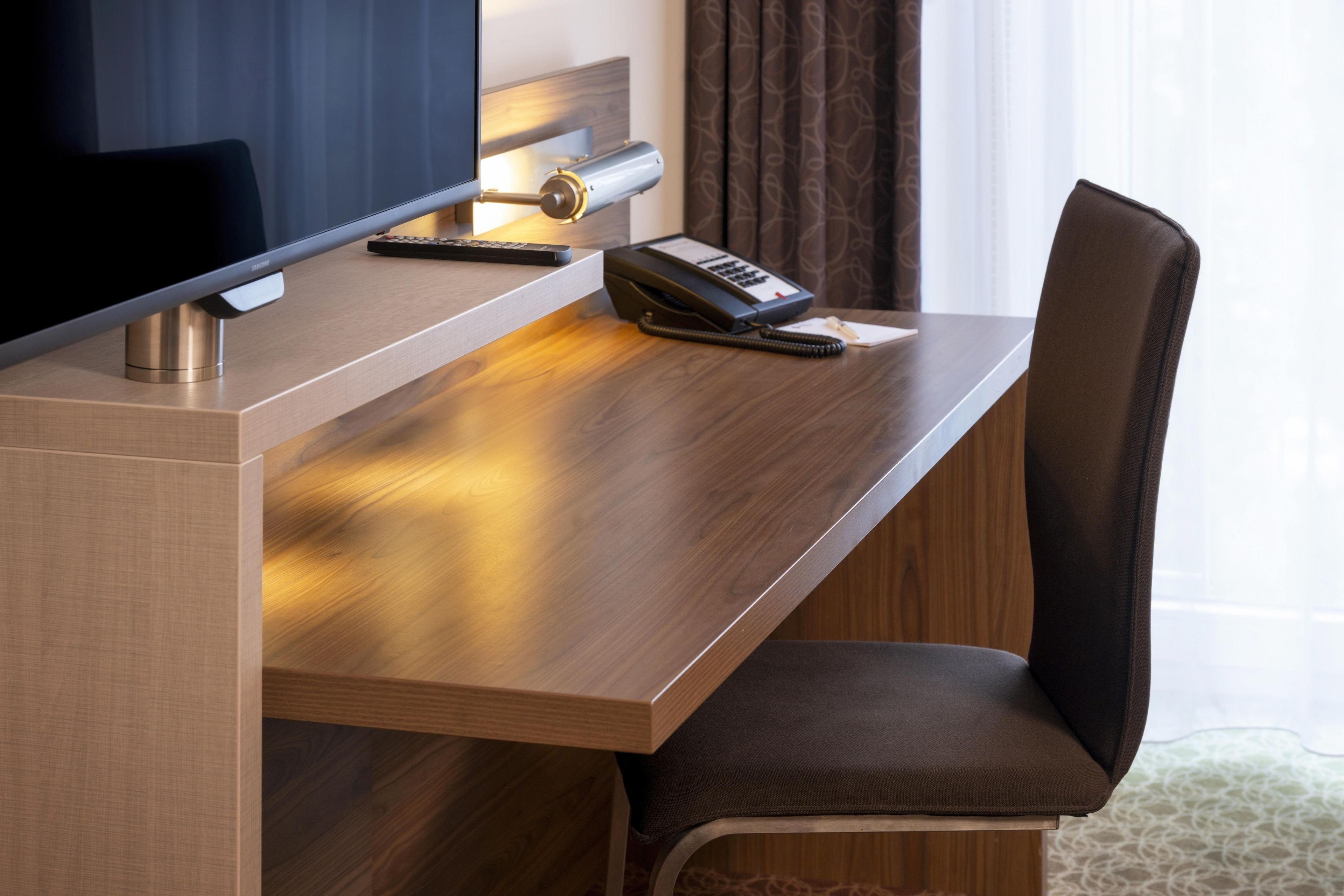 Ein Hotelzimmer mit einem Holztisch, einem Stuhl, einem Fernseher, einem Telefon und einer Fernbedienung.
