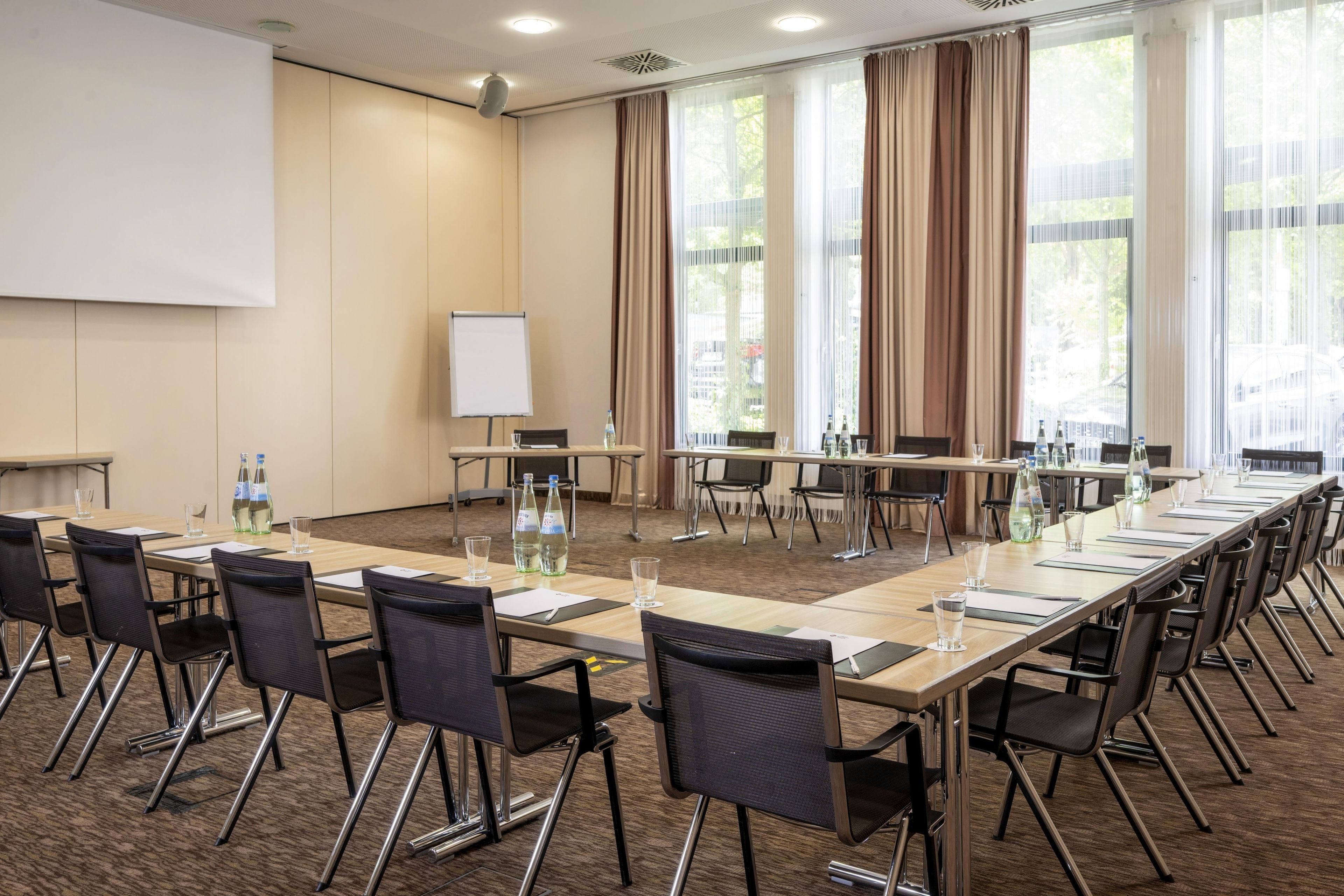 A conference room with a long table, chairs, a whiteboard, and large windows with curtains.