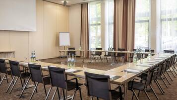 A conference room with a long table, chairs, a whiteboard, and large windows with curtains.