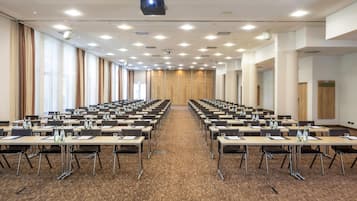 Ein Konferenzraum mit Tischen und Stühlen, einem Projektor und großen Fenstern mit Vorhängen.